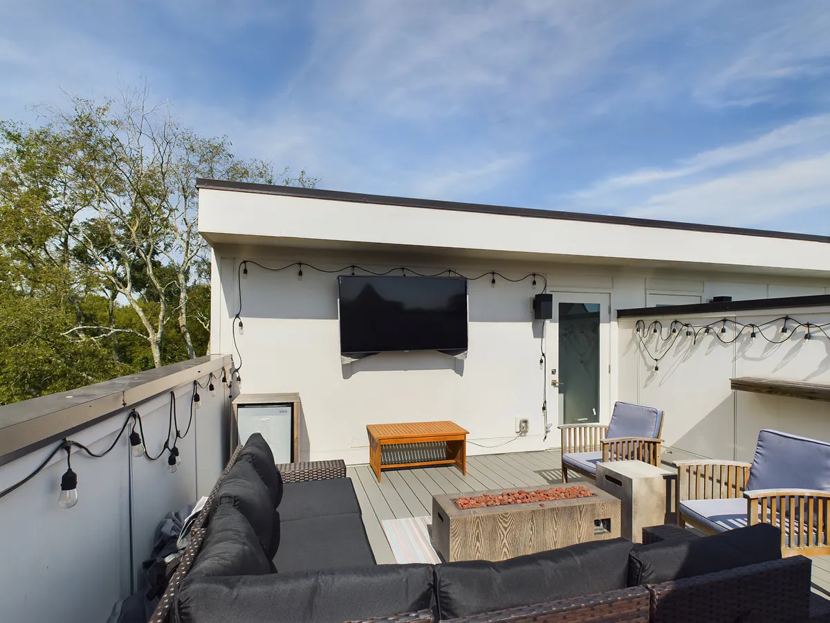 An inviting outdoor seating area on a rooftop deck, complete with decorative lighting, a coffee table, and a television screen. The space feels social and relaxing, ideal for unwinding and enjoying the city views after a night out.